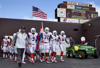 Head coach Scott Shafer leads his team onto the field as offensive lineman Ivan Foy (72) carries a flag.